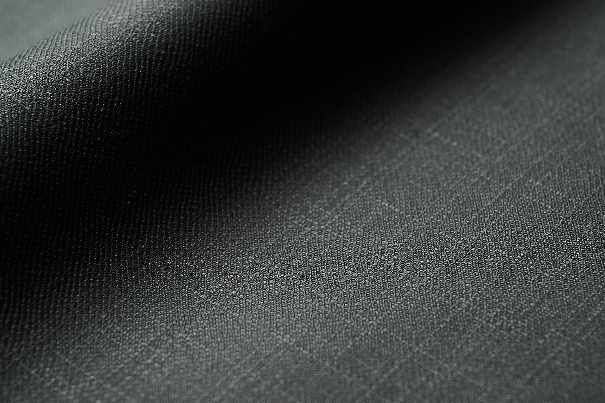 Close-up of dark grey woven wool fabric with a fine texture and soft folds in the shadows