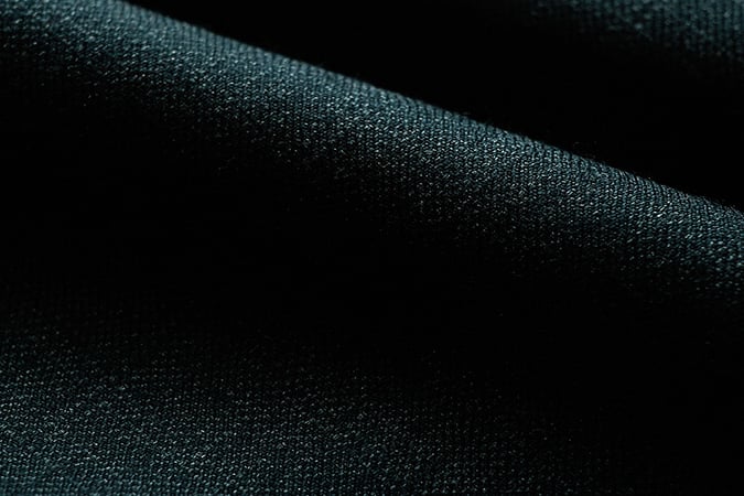 Close-up of dark green-black woven wool fabric with a visible fine texture, draped in soft folds
