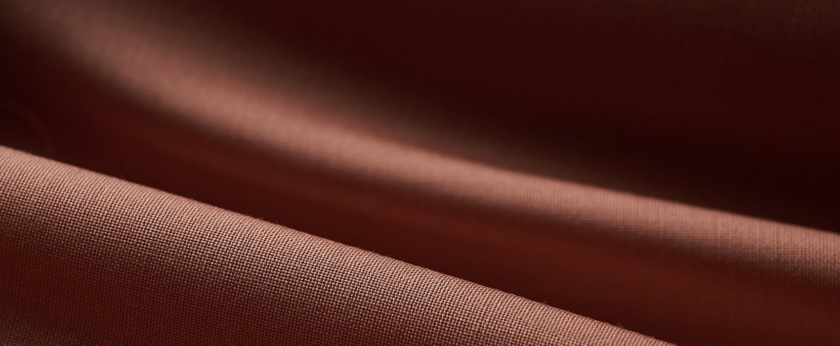 Close-up of soft brick-red woolen fabric with fine weave, draped in gentle folds and shadow