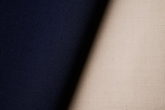 Close-up of two woven fabrics, one navy blue and one beige, overlapping diagonally