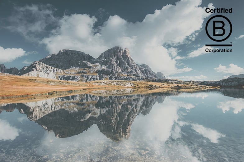 Rocky mountain reflected in a still lake under a cloudy sky, with the Certified B Corporation logo