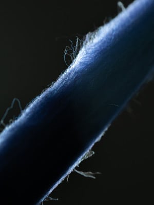 Close-up of a blue wool yarn with fine fibers catching the light against a dark background