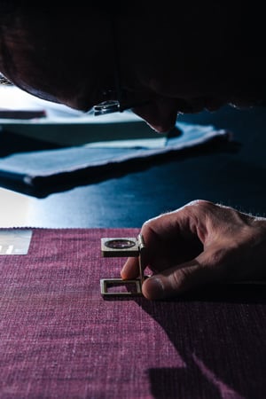 Man leans over a purple woven fabric, inspecting it with a folding thread counter magnifier.