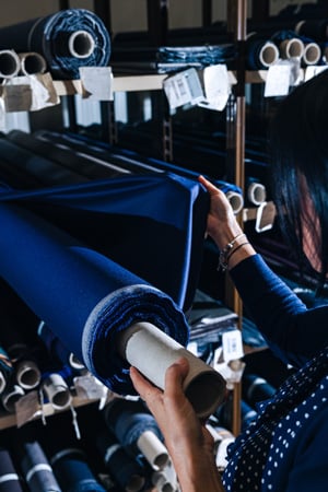 Woman holding a roll of blue fabric among shelves stacked with fabric rolls in a textile warehouse