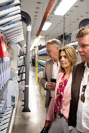 Three visitors look at textile machinery along a production line inside a wool mill.