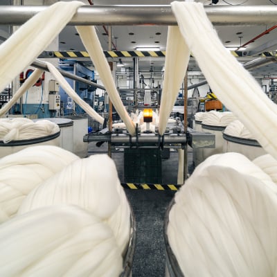 Thick strands of white wool sliver feeding from large containers into a machine in a textile mill
