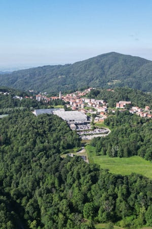 Aerial view of a village and large factory buildings among green wooded hills under a clear sky