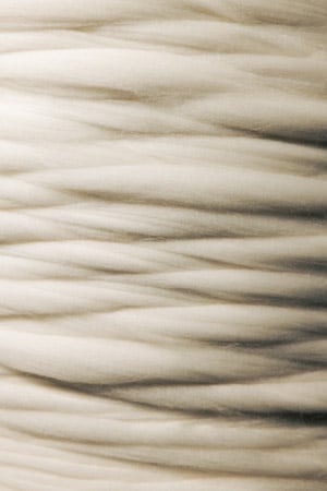 Close-up of thick, soft strands of cream-white wool roving layered in horizontal waves