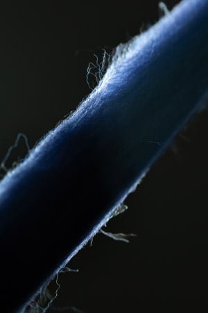 Close-up of a blue wool yarn on a dark background, with fine loose fibers lit along its edge