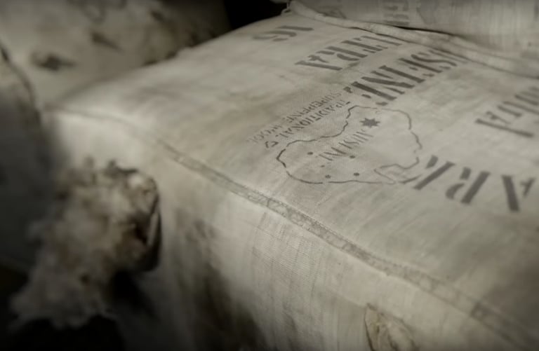 Burlap wool bale with a stenciled map and lettering, raw wool fibers poking out
