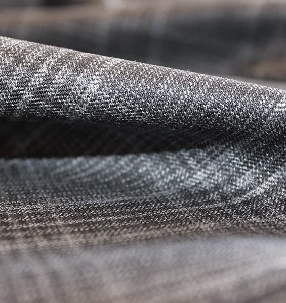 Close-up of a folded dark grey wool fabric with a subtle check pattern and visible twill weave