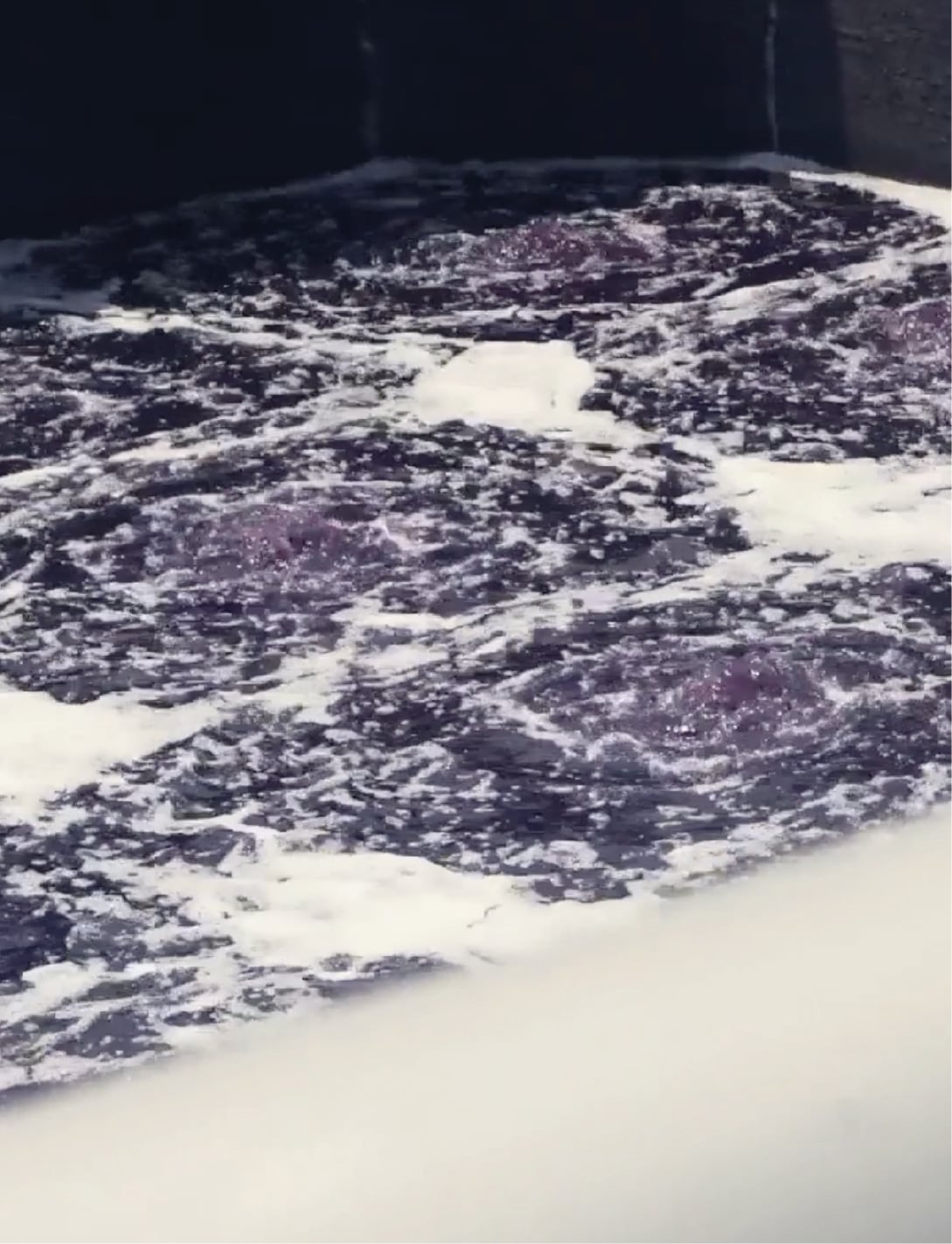 Dark blue-purple water churning with white foam inside a concrete basin