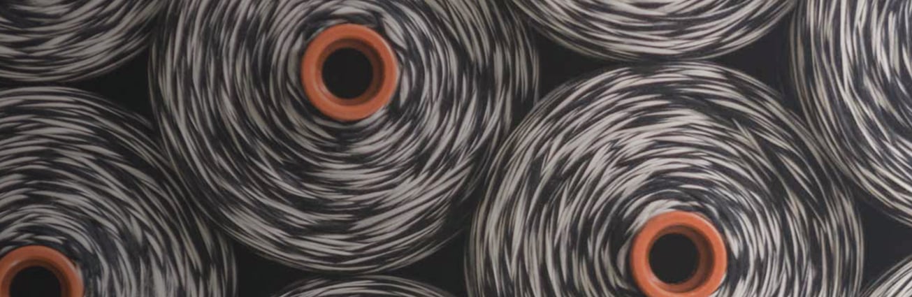 Close-up of spools of black and white mottled yarn with orange cores, arranged side by side