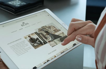 Hand touching a tablet screen showing the REDA website with fashion images of men in suits