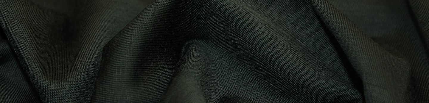 Close-up of dark green knit wool fabric draped in soft folds, showing its fine texture