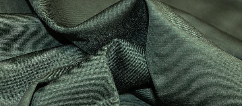 Close-up of dark green knit fabric draped in soft folds, showing its fine texture