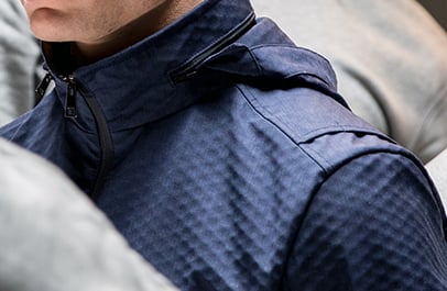 Close-up of a navy blue jacket with a textured diamond-pattern fabric, zipped collar and hood