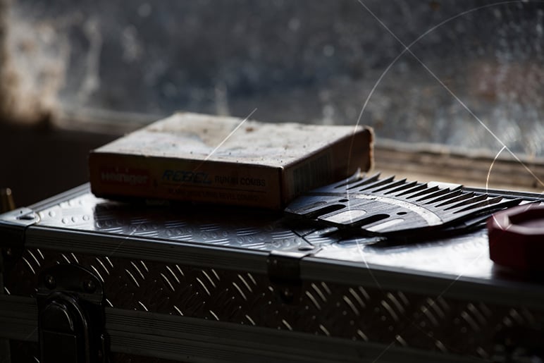 Box of Heiniger Rebel punch combs and a metal shearing comb on an aluminum case by a dusty window