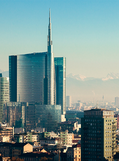 Glass skyscrapers with a tall spire rise above a city skyline, with snow-capped mountains in the distance.