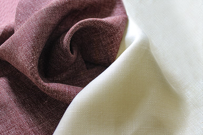 Close-up of burgundy woven fabric swirled in soft folds beside a smooth cream fabric