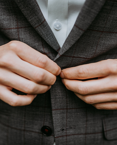 Close-up of hands buttoning a grey checked wool jacket worn over a white shirt