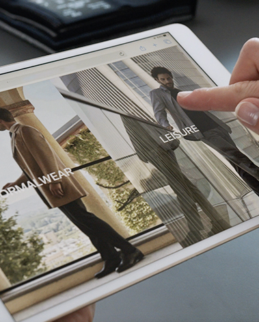 Finger touching a tablet showing menswear categories "Formalwear" and "Leisure" with models in coats