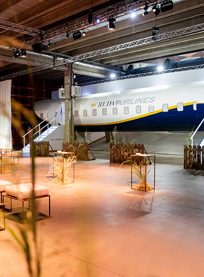 Event space in a hangar with a Reda Airlines plane fuselage, stairs, high tables and dried grass decor