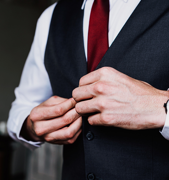 Man in a white shirt and red tie buttoning a dark grey wool waistcoat