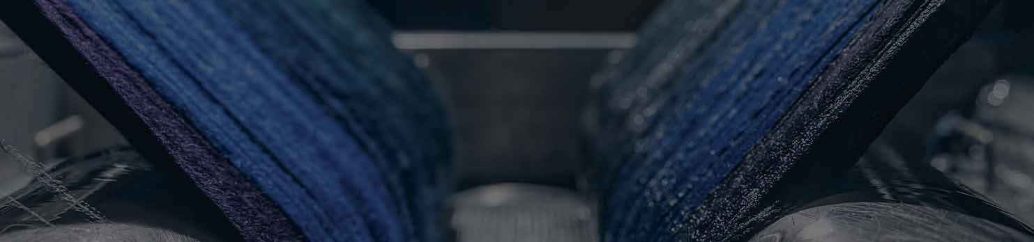 Close-up of blue wool yarn wound on large spools in a dimly lit textile machine