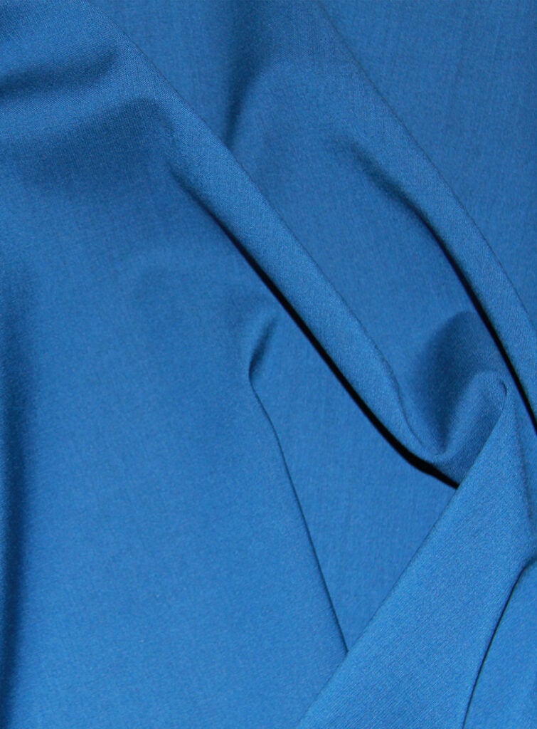 Close-up of draped blue wool fabric with soft folds and a fine, smooth weave