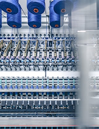 Blue yarn spools mounted above a textile machine with rows of threads running through its mechanisms