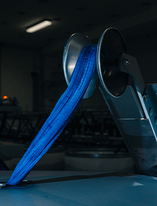 Blue fabric band running over a metal roller on a textile machine in a dark industrial room