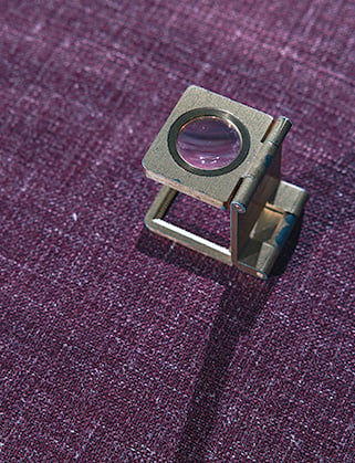 Brass folding thread counter magnifier standing on a purple woven wool fabric