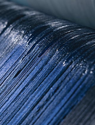 Close-up of deep blue wool fabric with fine vertical texture and glossy, light-catching fibres