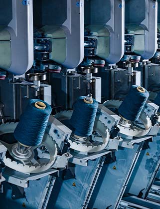 Blue yarn bobbins on a row of industrial textile machines in a spinning mill