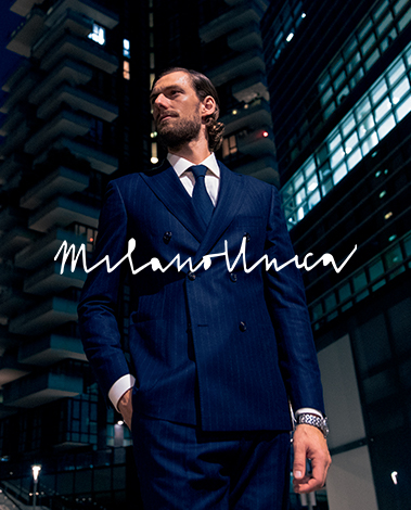 Man in a navy pinstripe double-breasted suit and tie at night among skyscrapers, Milano Unica logo