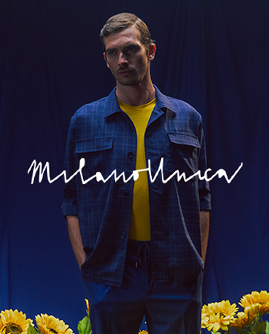 Man in a blue checked overshirt and yellow tee among sunflowers; Milano Unica logo