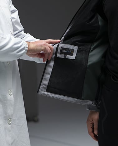 Person in a white lab coat touches the mesh lining and Reda Active label of a dark jacket