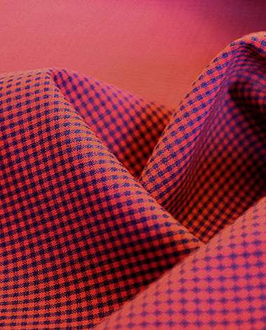 Close-up of draped red and navy micro-gingham fabric with soft folds against a pink background