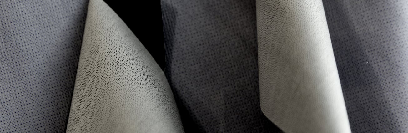 Close-up of grey fabric sheets with a fine dotted texture, curled over a dark grey textile background