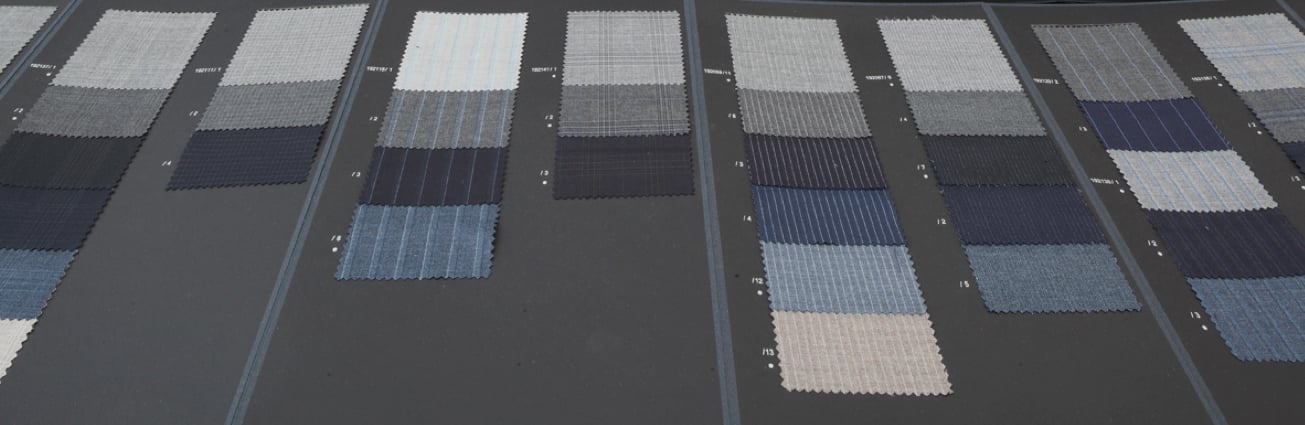 Rows of wool fabric swatches in grey, navy and blue, with stripe and check patterns, on a dark surface
