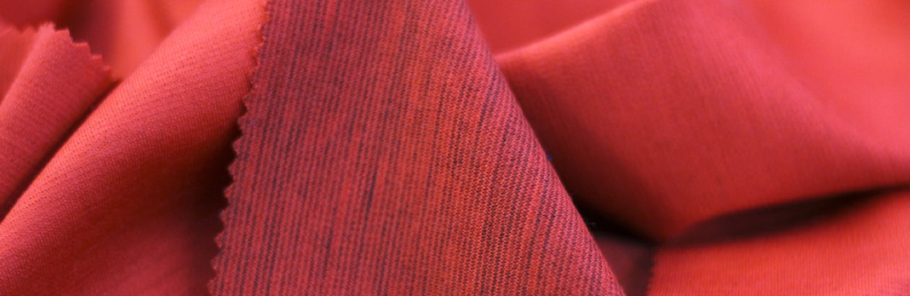 Close-up of red woolen fabric with soft folds and a visible fine diagonal texture and cut edge