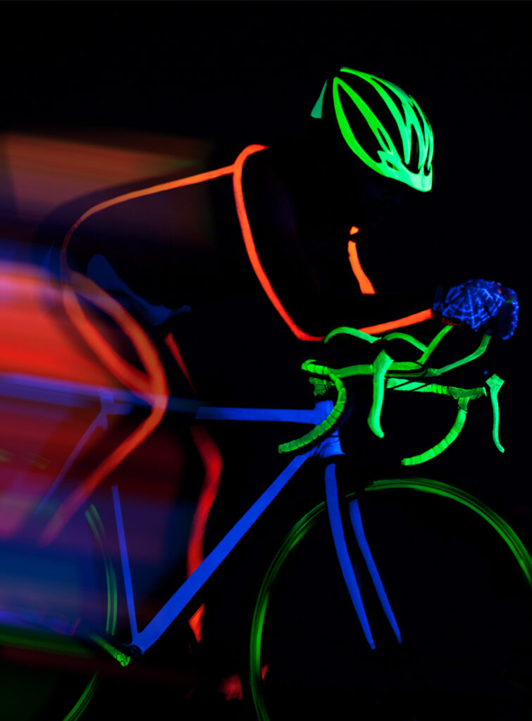 Cyclist in fluorescent outline, helmet and bike glowing under UV light in the dark, with motion blur