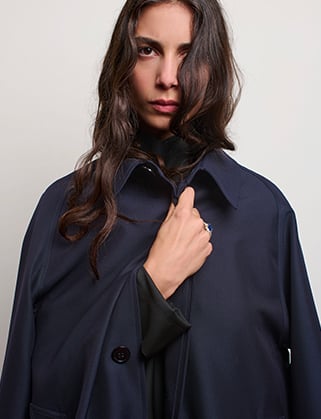 Woman with long wavy dark hair wearing a navy coat over a black garment, hand held at her collar