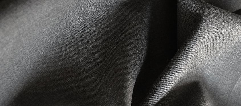 Close-up of dark grey woven fabric with soft folds and shadows, showing a fine, smooth texture