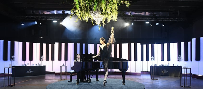 Ballerina in standing split beside a pianist at a piano on a Reda stage with giant keys