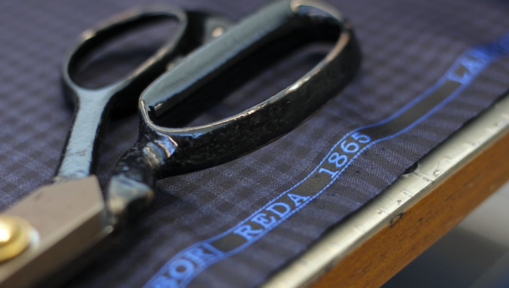 Black tailor's shears on checked blue wool fabric with a Reda 1865 selvedge on a wooden cutting table