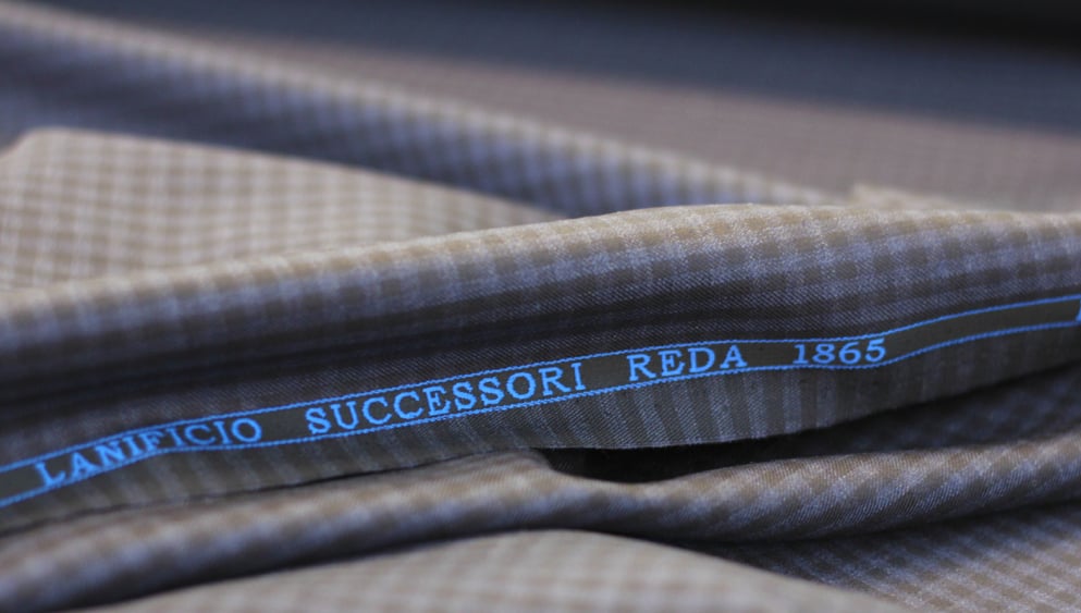 Folded brown and blue checked wool fabric with a blue selvedge reading "Lanificio Successori Reda 1865"