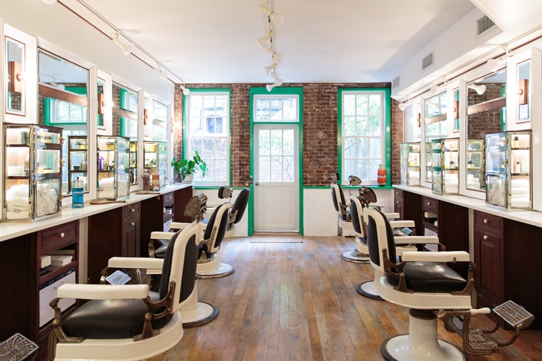 Vintage barbershop with white and black leather chairs, wood counters, mirrors and a brick wall with green frames