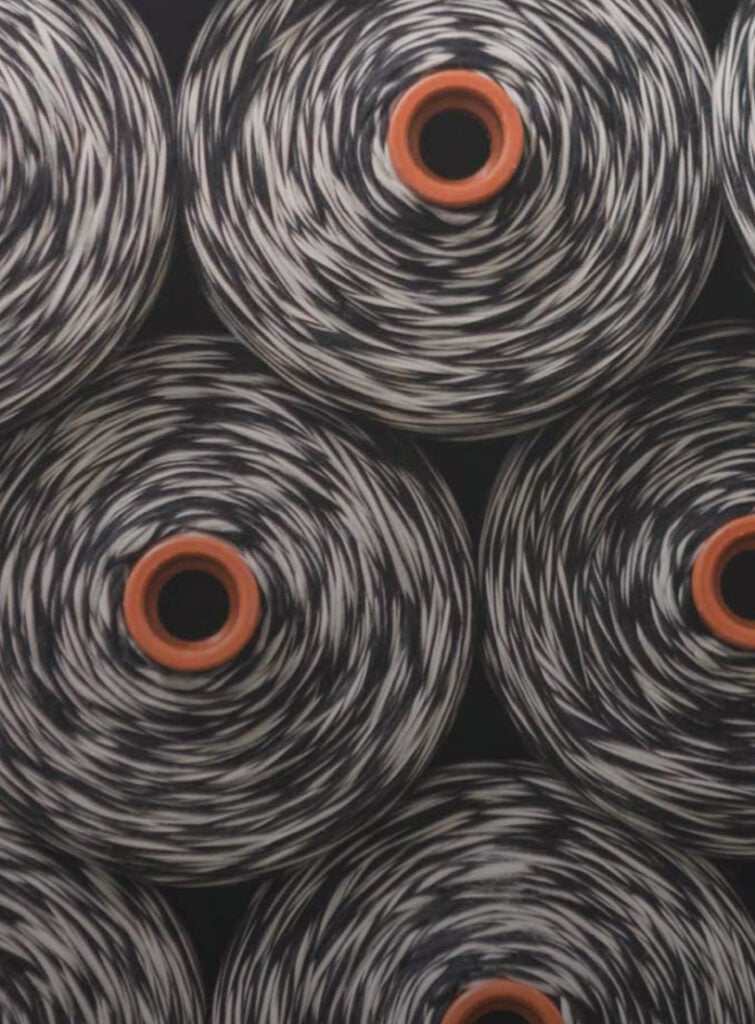 Close-up of black and white wool yarn cones with orange centers, stacked side by side